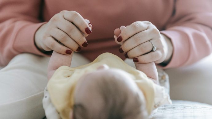 Ženské ruce drží za ruce miminko.